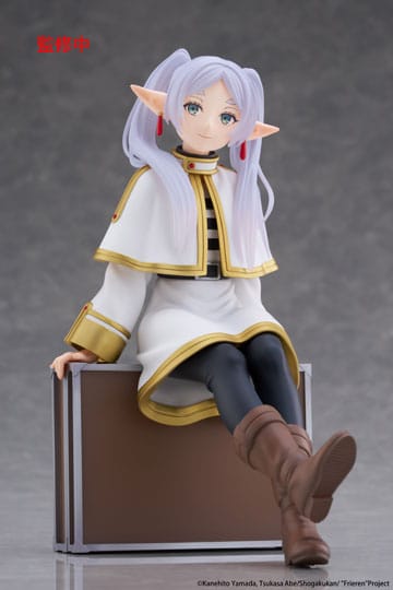 Figurine of a character with white hair and pointed ears sitting on a box against a gray background.