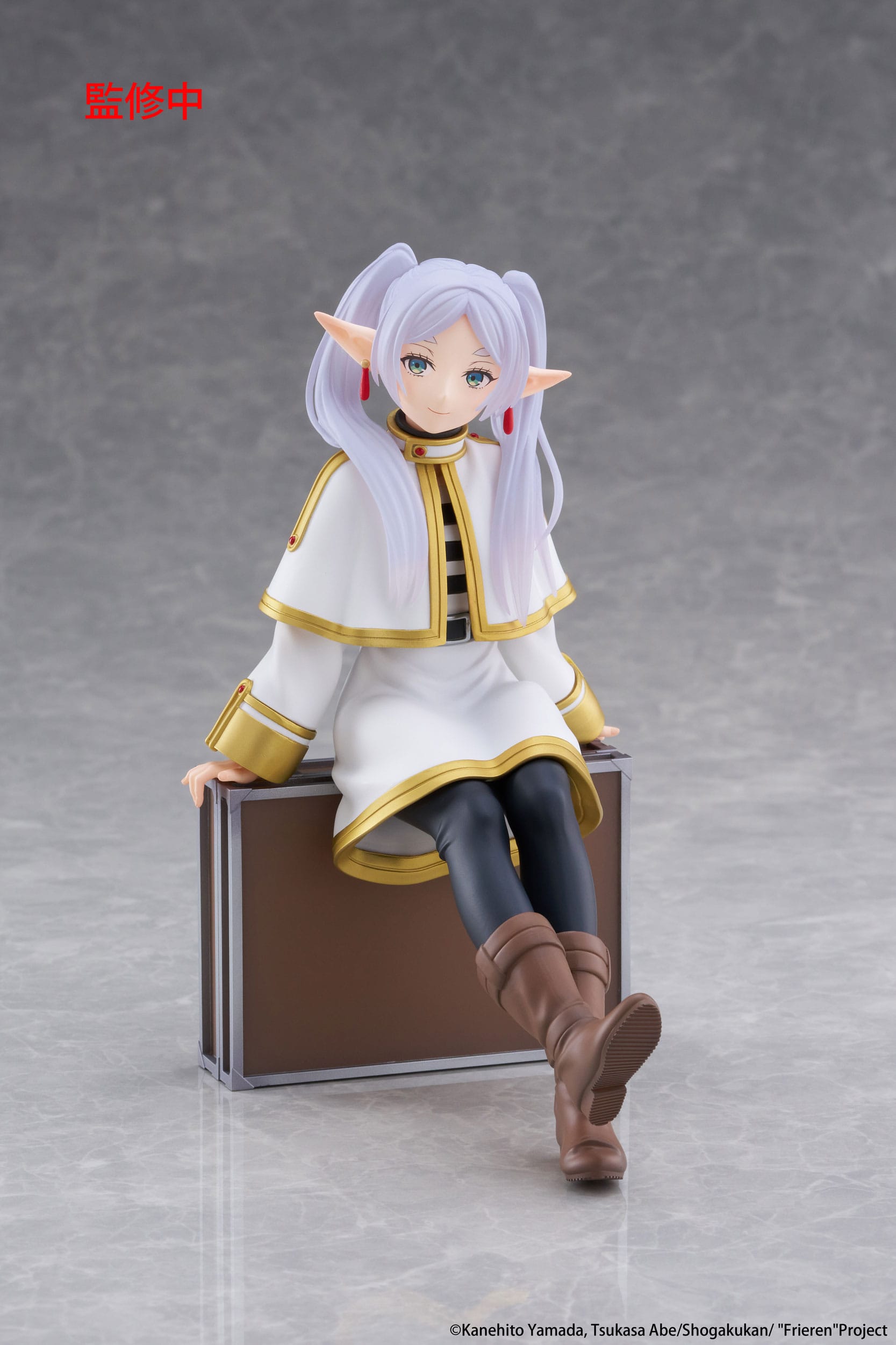 Figurine of a character with white hair and elf-like ears sitting on a suitcase.