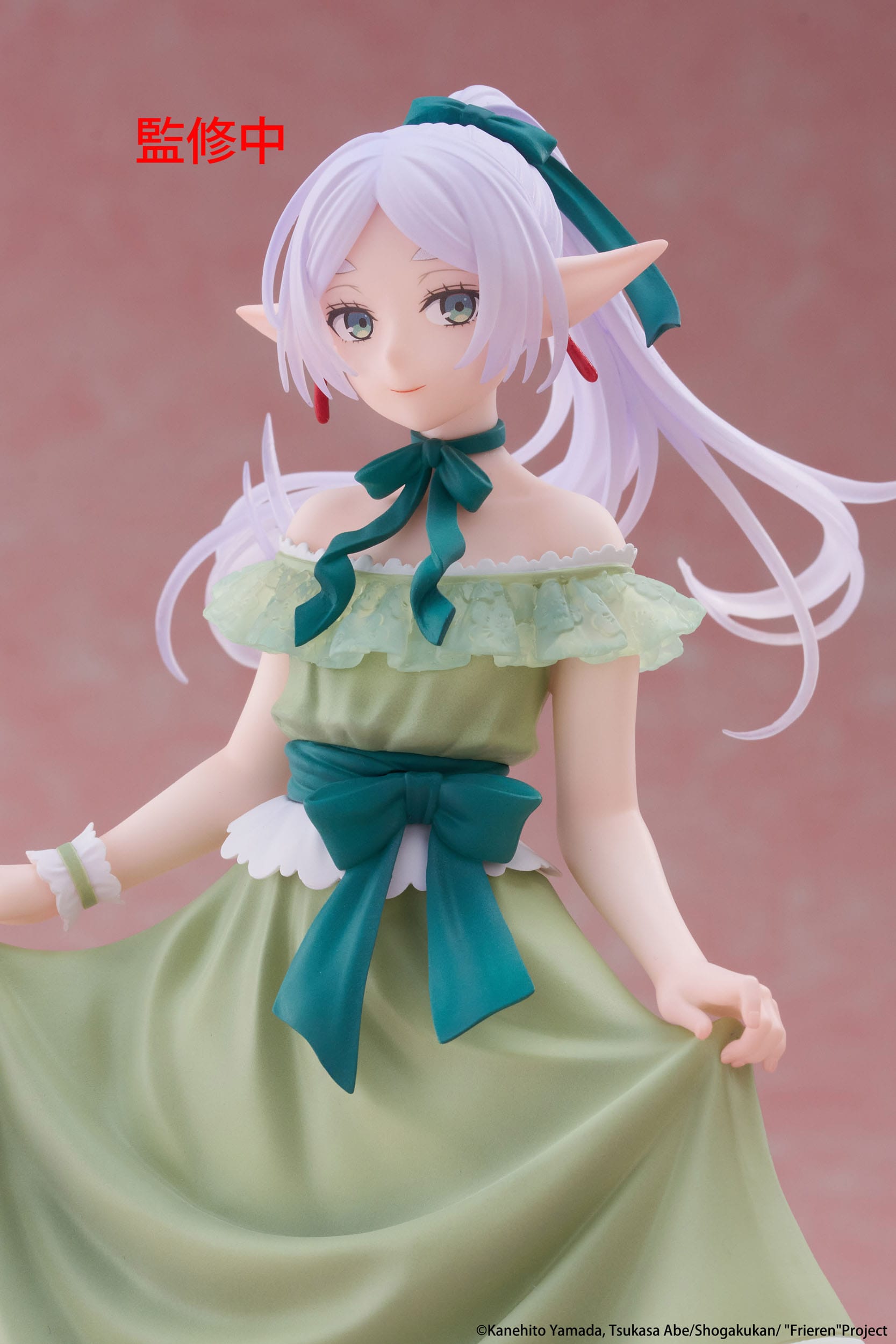 Anime character figurine with green dress and white hair against a pink background