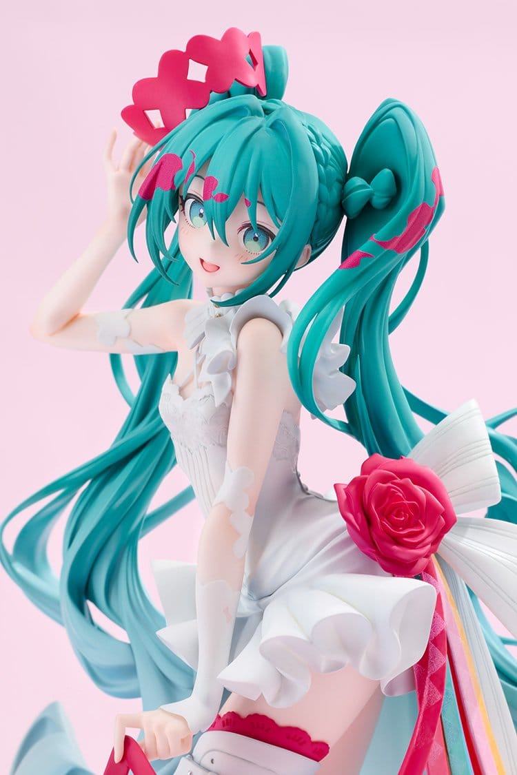 A collectible figurine of Hatsune Miku in a white and pink outfit with her signature teal twin-tails, posed against a solid light pink background.